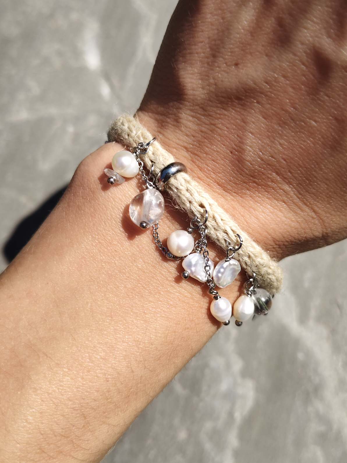 Frau trägt handgestricktes Seide-Hanf-Armband mit Bergkristall und Perlen am Handgelenk, fotografiert im Sonnenlicht
