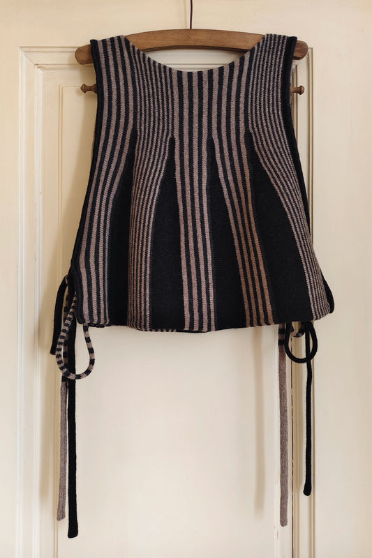 Ein ausdrucksstarkes Stricktop mit grafischem Streifenmuster und skulpturaler Silhouette, in Schwarz, Beige und Anthrazit.